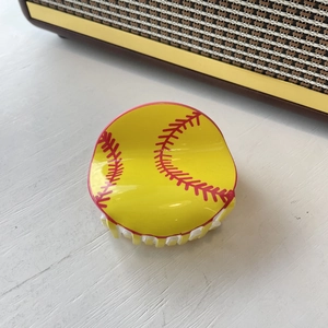 Detail of yellow softball hair claw clip with red stitching on wood surface