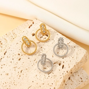 Close-up of gold and silver twisted rope earrings with three zircon stones on stone