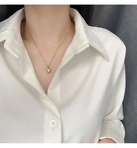 Detail of a French-style gold pearl necklace on a model with a white shirt