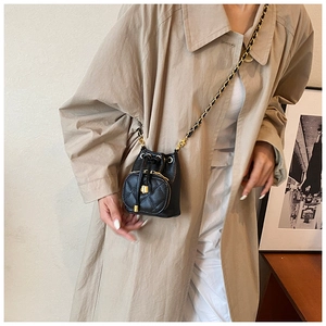 Close-up of black quilted bucket bag with chain strap on khaki trench coat model