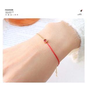 Detail of a red woven bracelet with a gold-plated circular red stone setting on the wrist
