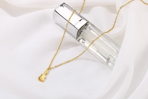 Gros plan d'un collier pendentif violon doré présenté sur un flacon en verre et de la soie