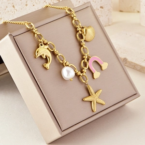 Golden ocean-themed necklace with starfish, dolphin and pearl charms on textured stone