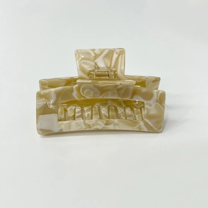 Macro detail of marble pattern hair claw clip with golden metal spring on white background