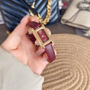 Detail of a rectangular gold case watch with a textured dark red leather strap