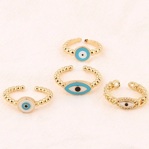 Detailed view of four gold evil eye rings with blue dripping oil on textured background