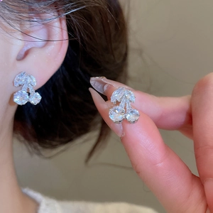Detail of silver cherry stud earrings with sparkling cubic zirconia on model's ear