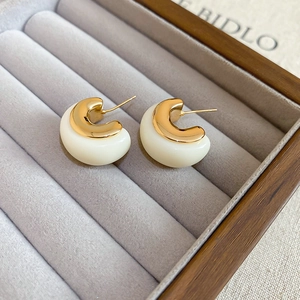 Close-up of vintage C-shape earrings in gold and cream resin on a grey velvet jewelry tray