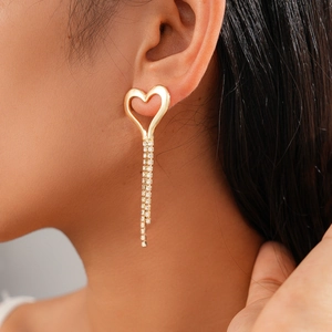 Close-up of golden hollow heart earrings with shimmering tassel rhinestones on model