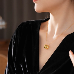 Dettaglio del ciondolo cilindrico dorato con stelle su collana in acciaio al titanio indossata