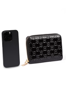 Detailed view of black patent leather coin purse with embossed pattern and gold zipper next to phone