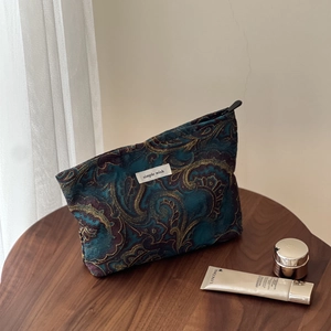 Detailed shot of dark blue paisley jacquard cosmetic bag with gold floral patterns