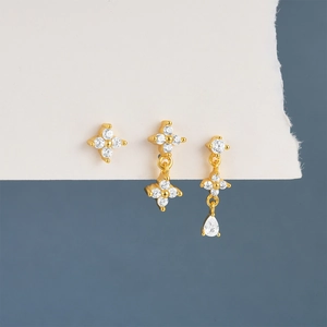 Detailed shot of three gold flower earrings with clear zircon on a blue backdrop