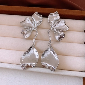 Détail de boucles d'oreilles fleurs argentées à texture plissée dans un écrin