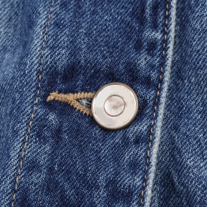 Macro shot of a vintage metal button on blue denim fabric with yellow contrast stitching