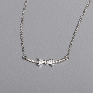 Detail view of a silver bow necklace featuring shimmering cubic zirconia on a gray surface