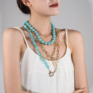 Detail of layered turquoise beaded chain and chunky gold link necklace on model