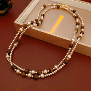 Détail du collier double rang avec perles blanches, pierres œil de tigre et fermoir doré
