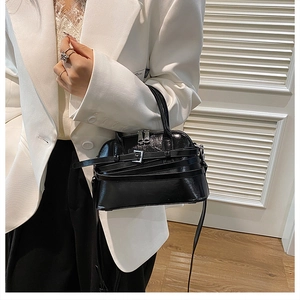 Detail of glossy black crossbody shell bag with double zippers and belted decor