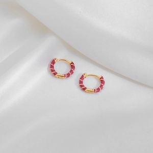 Detail of gold-plated hoop earrings with magenta enamel spiral pattern on white silk