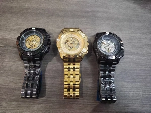 Three skeleton automatic mechanical watches in gold and black on a textured wood surface