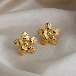Detailed close-up of gold flower earrings with brushed metal petals on white silk fabric