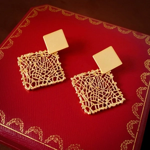Detailed close-up of golden square mesh earrings on a luxury jewelry box