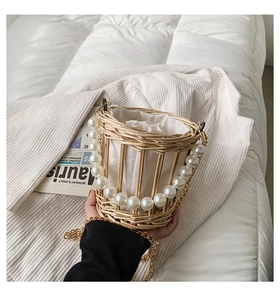 Detail of woven straw bucket bag featuring large pearl handle and metal chain strap