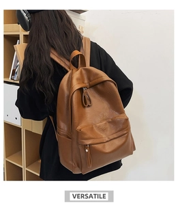 Close-up of a brown PU leather backpack being worn in front of a wooden bookshelf