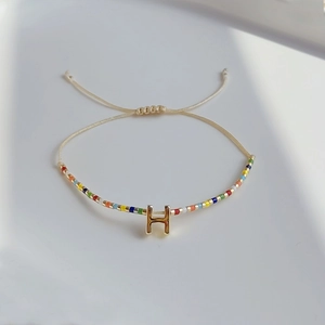 Detail eines Miyuki-Perlenarmbands mit goldenem Buchstaben H und bunten Perlen im Boho-Stil