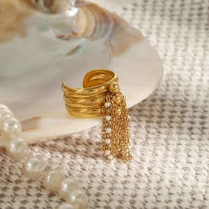 Dettaglio dell'anello in oro con perle e lunghe nappe su sfondo a conchiglia