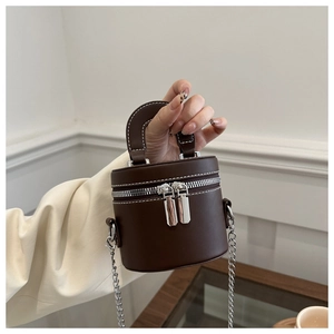 Détail d'un mini sac cylindre marron foncé avec coutures blanches et chaîne en argent