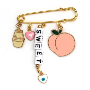 Detailed shot of golden safety pin brooch featuring sweet milk and evil eye pendants