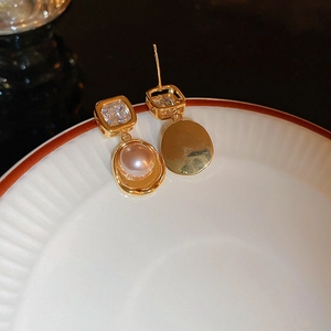 Detailed macro view of gold-plated square zircon earrings with pearl drop on white tray