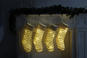 Detail of four lit knitted Christmas stockings with fish scale pattern on white mantel