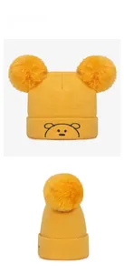Détail du bonnet tricoté jaune pour bébé avec pompons et broderie d'ours mignonne