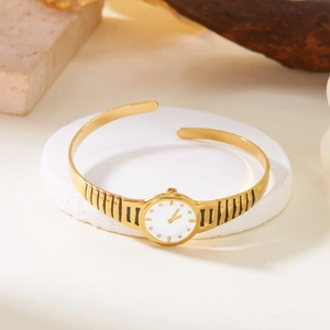Detailed view of golden watch-style open bangle on a white marble display tray