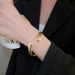 Close-up of golden open cuff bracelet with polished teardrop ends on a suit sleeve
