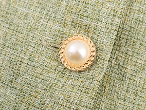 Macro shot of gold pearl button on green tweed fabric jacket detail and texture