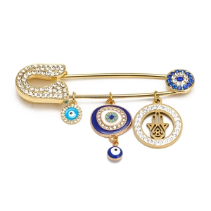Detailed view of golden safety pin brooch featuring Hamsa Hand and Evil Eye charms with crystals