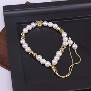 Detail of adjustable pearl bracelet with golden heart charm on a black display tray