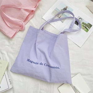 Flat lay of pink and purple canvas tote bags with croissant print and lifestyle props