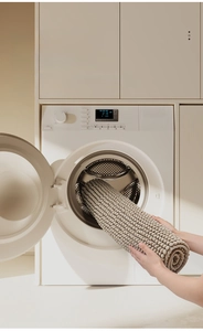 Close-up of machine washable beige chenille rug being placed in a front-load washer