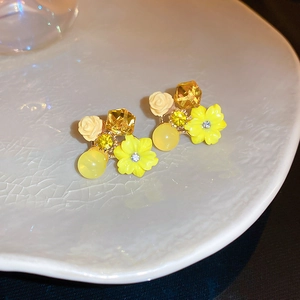 Close-up of yellow floral stud earrings with crystals on a white ceramic plate