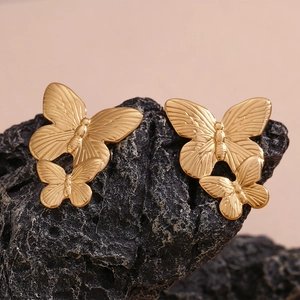 Macro detail of gold-plated stainless steel double butterfly earrings on black stone