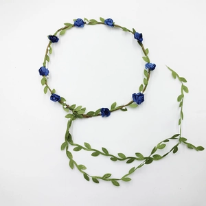 Close-up of a floral headband with blue fabric flowers, green leaves and hanging vines