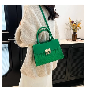 Detail of emerald green crocodile texture handbag with gold geometric buckle on model