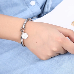 Detail of silver cable bracelet with relief pendant worn by a model in casual setting