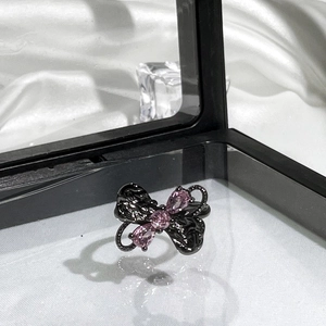 Close-up of black butterfly ring with three pink gemstones on white silk background