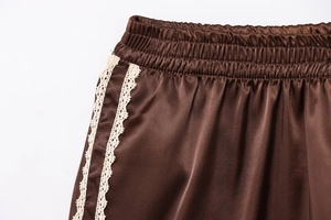Detailed close-up of brown satin shorts featuring white lace trim and elastic waistband